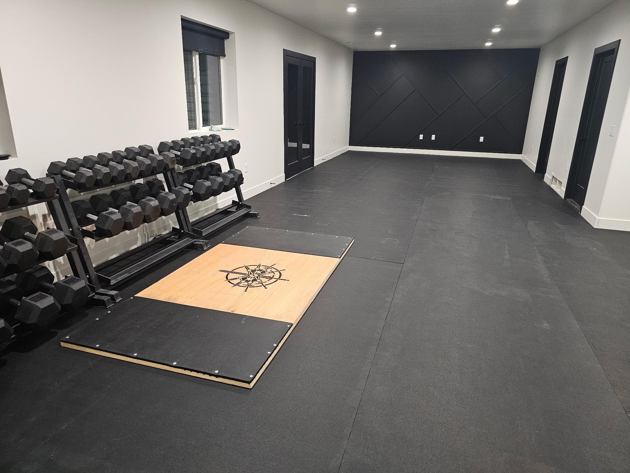 Finished basement home gym with rubber flooring, dumbbell racks and lifting platform