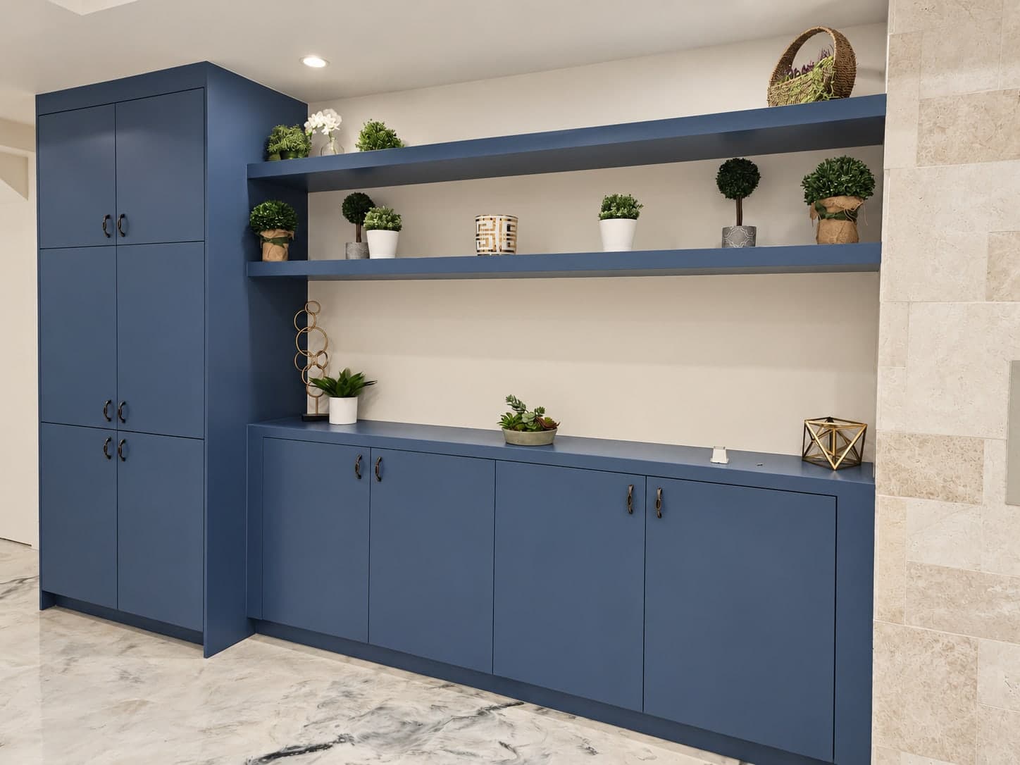 Blue built-ins with a tall cabinet, two floating shelves and a run of base cabinets, beside a stone tile wall