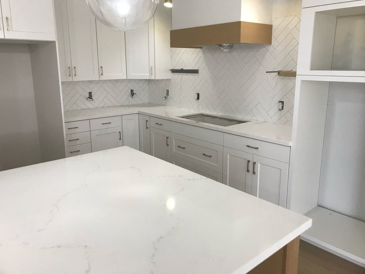 Kitchen in progress with white cabinets, a pale island countertop and herringbone tile backsplash