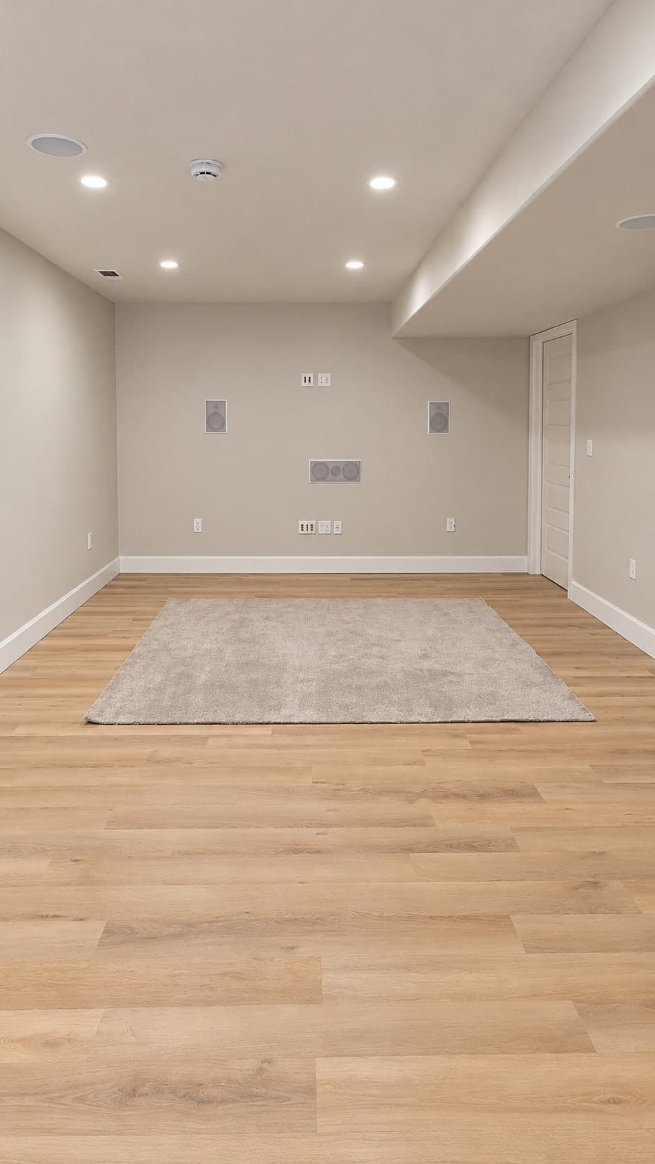 Basement media room with plank flooring and a rug, in-wall left, center and right speakers, ceiling speakers and media wall plates, under recessed lights