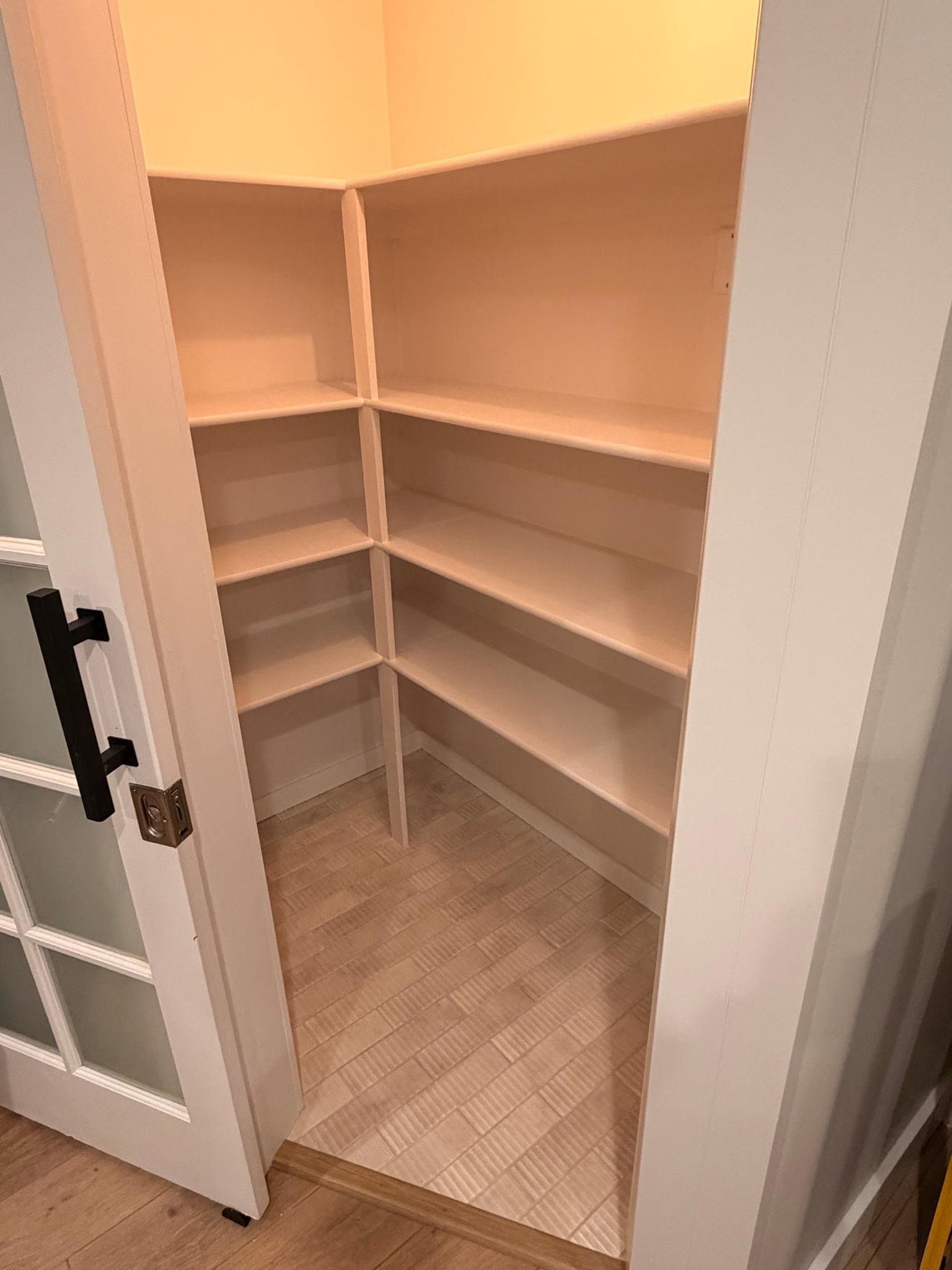 Walk-in pantry with painted wraparound shelving and glass-panel door