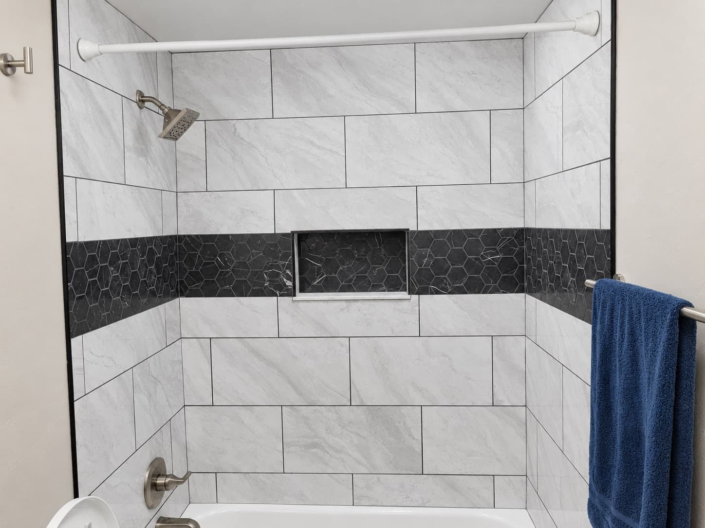 Tub and shower surround in large gray marble-look tile, with a black hexagon mosaic band and a recessed niche set into the band