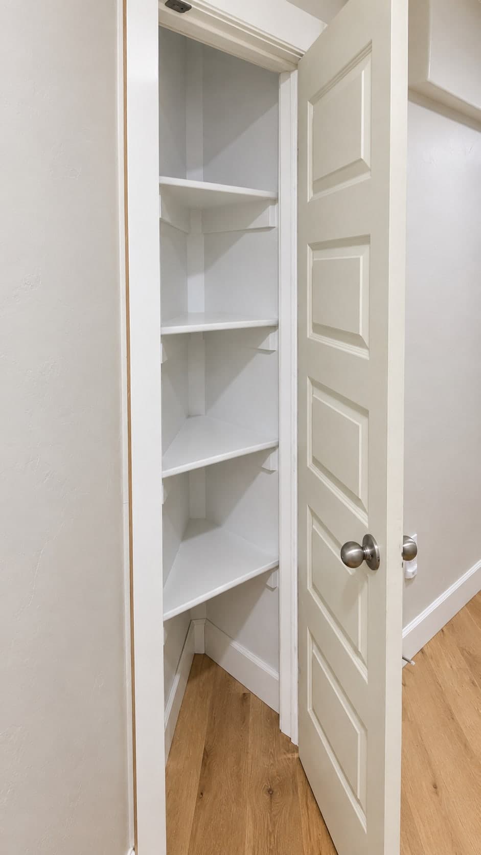 Corner closet with white built-in shelves behind a paneled door