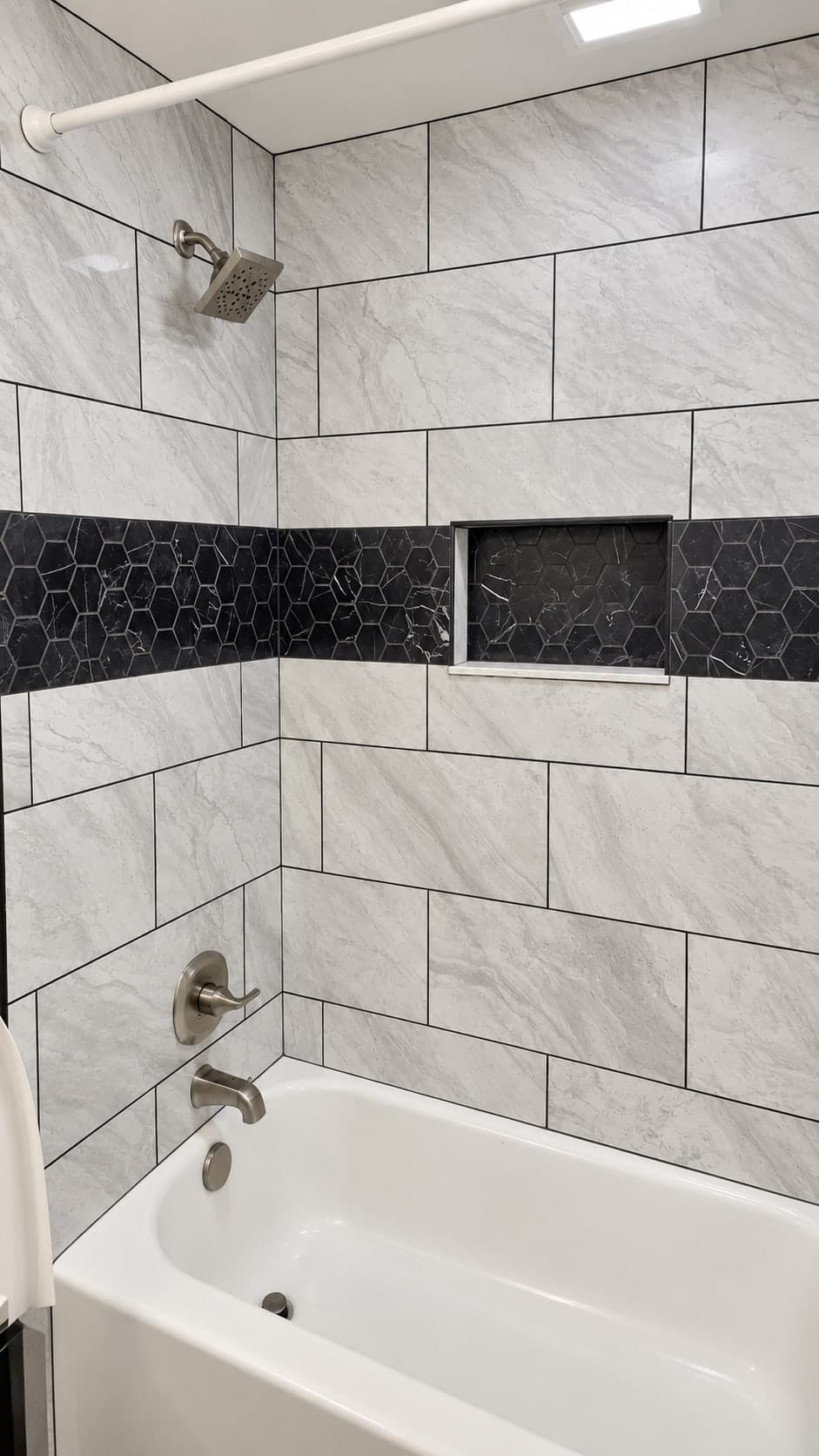 The gray tile tub surround seen from the end of the tub, with the black hexagon band, the niche, the valve and the spout